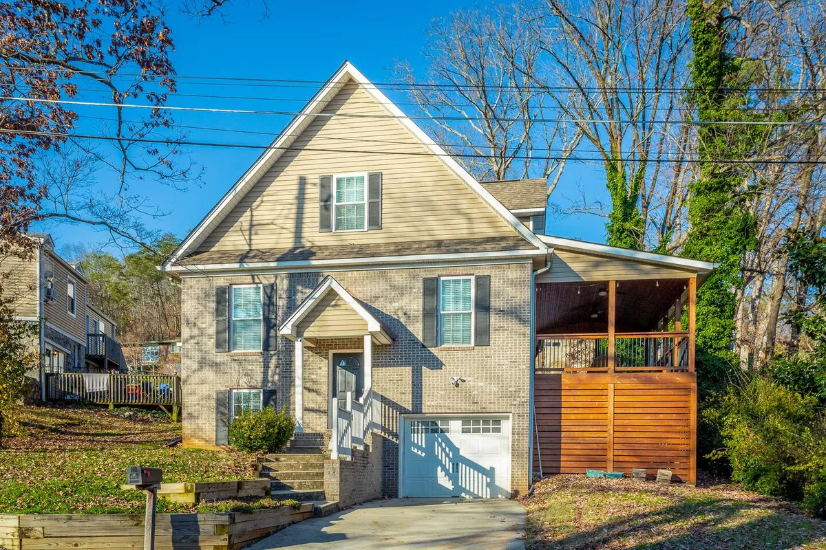 A beautifully maintained brick single-family home with a welcoming front porch, large windows, and a lush landscaped yard. The porch is set up for sunset views and perfect for morning coffee, offering a relaxing spot surrounded by greenery. The overall mood is warm and inviting, ideal for outdoor gatherings or family barbecues.