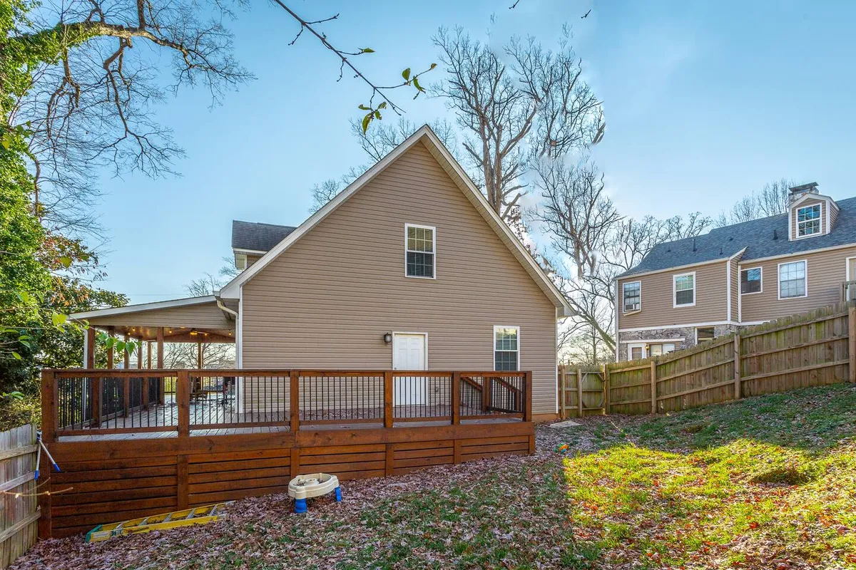 This image presents a wide view of the home's wooden deck overlooking a fenced backyard, framed by greenery. The space is set up for outdoor gatherings and family barbecues, with ample room for kids to play or adults to unwind after a day of adventures.