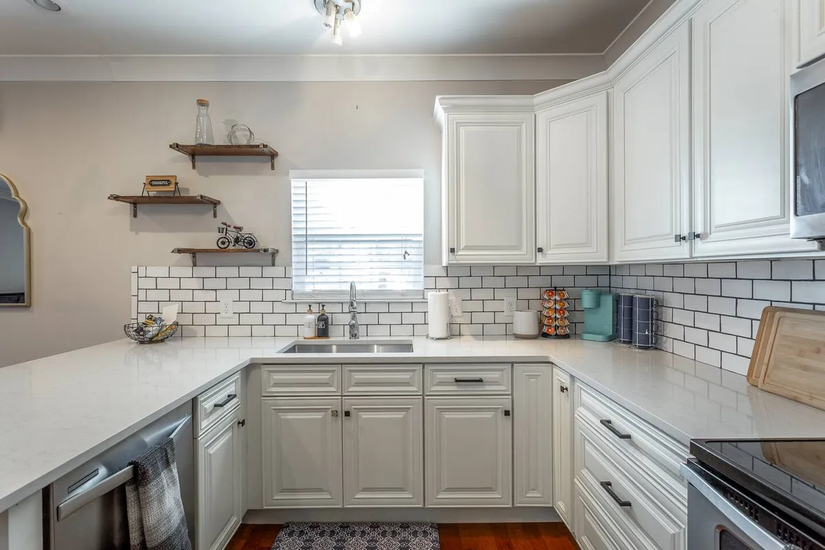 A bright kitchen with white cabinetry, marble countertops, and a subway tile backsplash. Abundant natural light streams in through the window, illuminating the spacious counters—ideal for group meal prep and social gatherings.