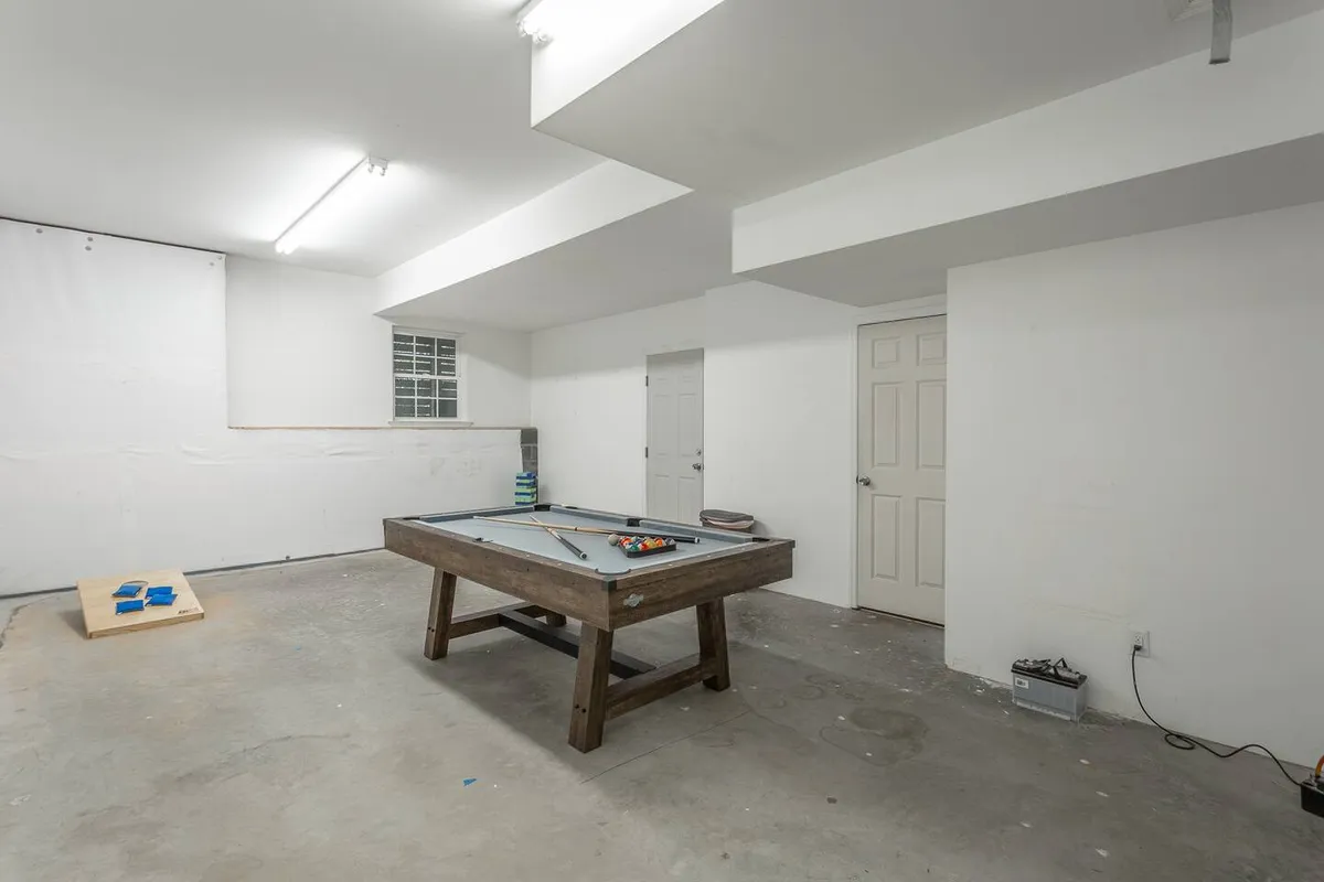 A dedicated game area highlighted by a pool table at the center, with doors in the background and a concrete floor. The setting is casual and inviting, ideal for friendly competitions and shared fun.