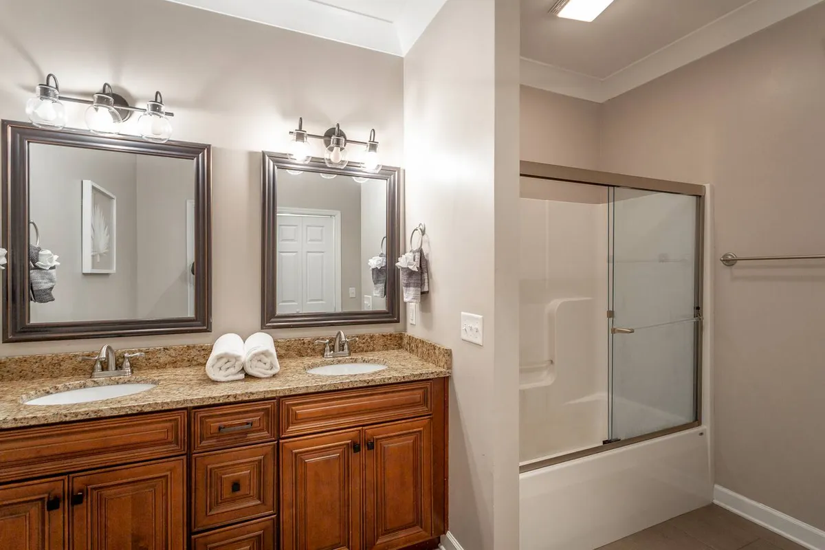 A modern bathroom with a double vanity, granite countertops, two large mirrors, and a bathtub-shower combo. The space is bright, organized, and calming—ideal for ensuring smooth routines for multiple guests.