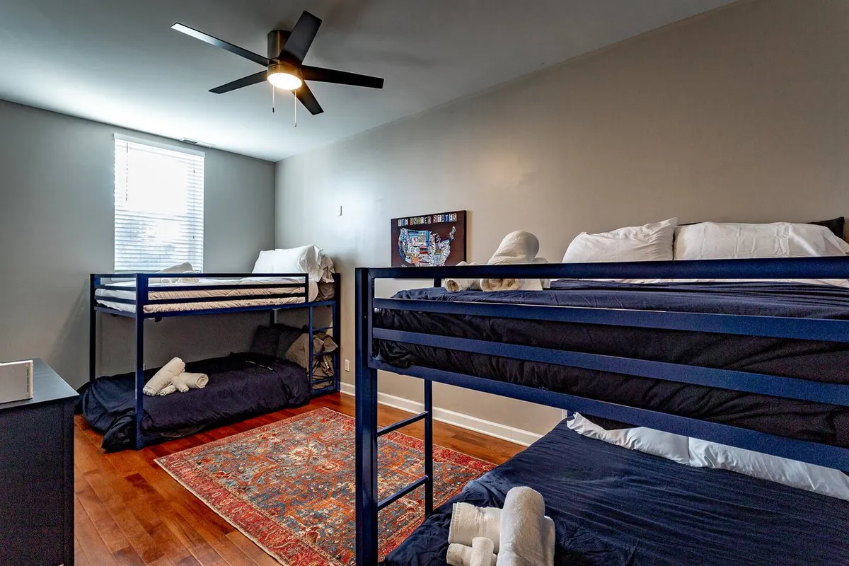 A playful bedroom with bunk beds, a window streaming in natural light, and a colorful area rug below. The room feels both fun and comfortable, perfect for children or friends enjoying time together.
