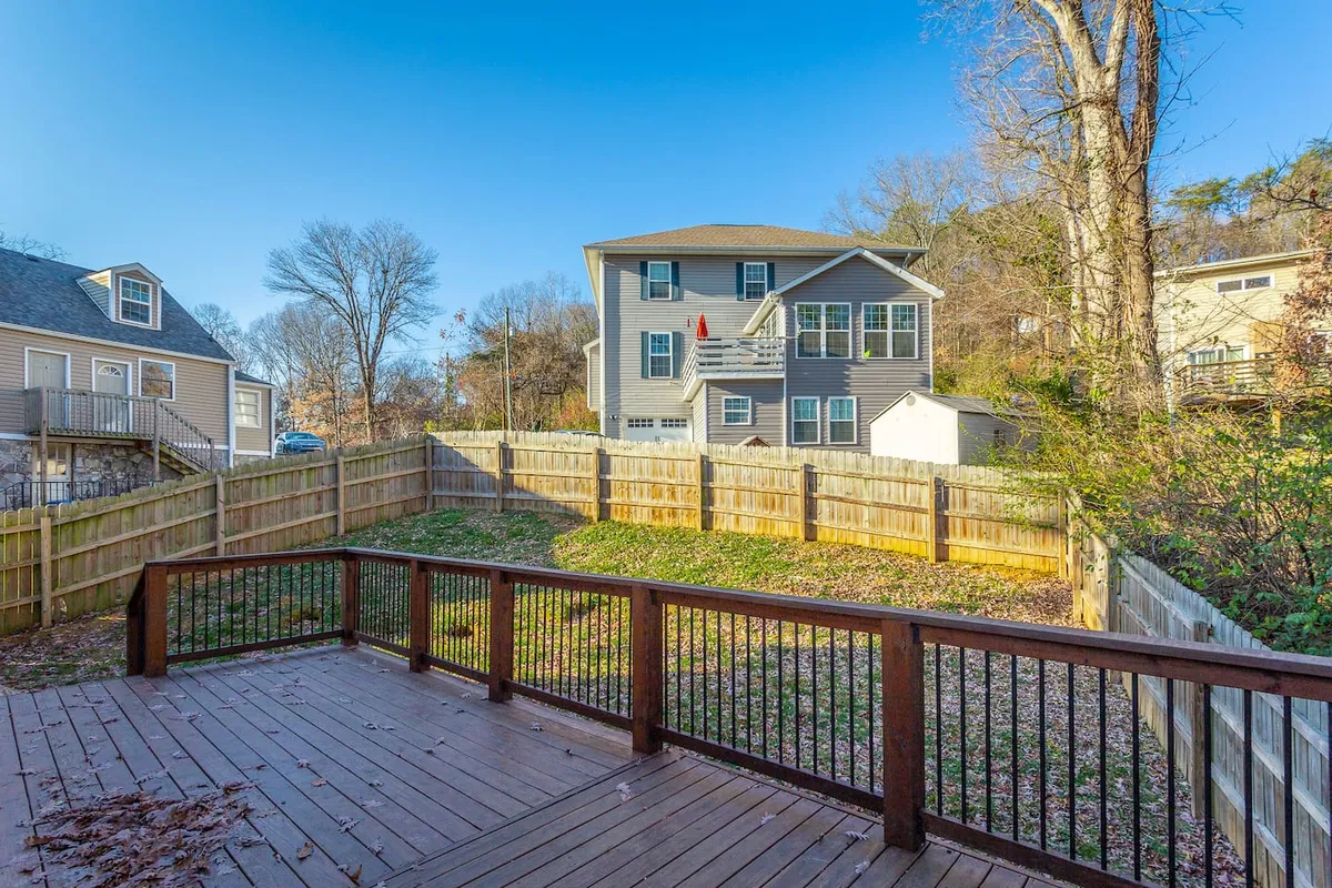 This image shows a spacious wooden deck attached to the house, overlooking a fenced yard with plenty of green space. The house facade is visible, and the deck is ideal for outdoor gatherings, barbecues, or informal meetings, providing a relaxing outdoor environment.