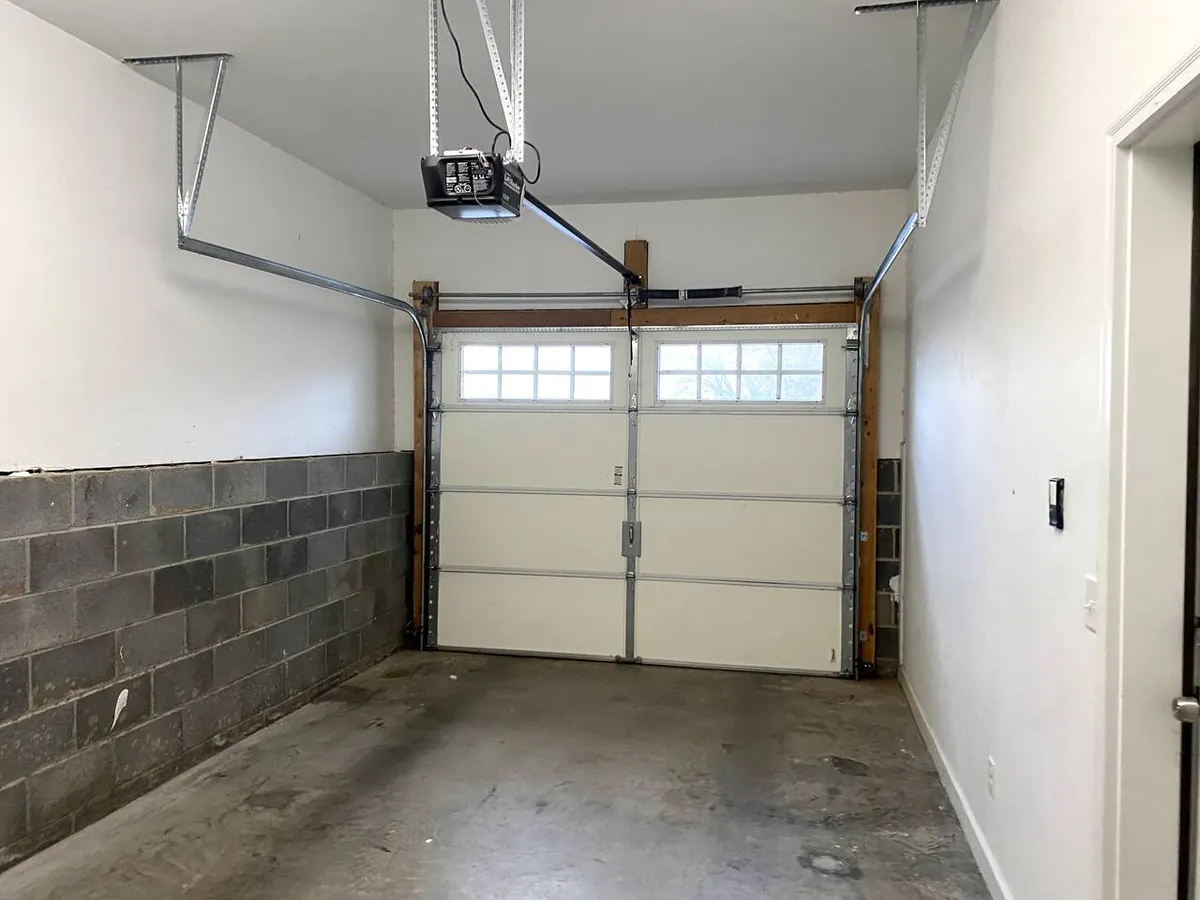 A view inside a clean, modern garage with a prominent garage door, ceiling-mounted opener, and concrete flooring—ready for secure and convenient parking.