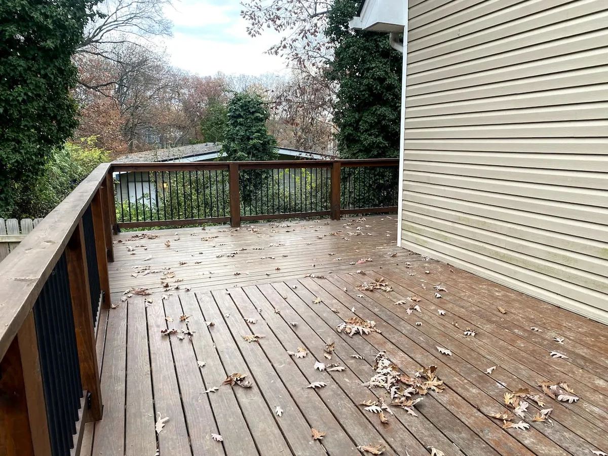 A peaceful exterior view of a wooden deck surrounded by lush greenery, with ample space for outdoor relaxation and gatherings. The scene evokes a sense of tranquility and togetherness, drawing attention to the opportunity to enjoy the outdoors right at home.